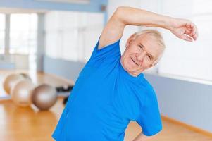 hombre mayor activo. alegre anciano haciendo ejercicios de estiramiento y sonriendo mientras está de pie en el interior foto