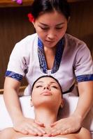 SPA serenity. Confident Thai massage therapist massaging beautiful young woman lying on massage table and keeping eyes closed photo