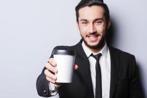 Charge yourself Portrait of confident young man in formalwear looking at camera and stretching out a cup of coffee while standing against grey background photo