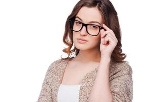 Confident beauty. Confident young woman adjusting her eyeglasses while standing isolated on white photo