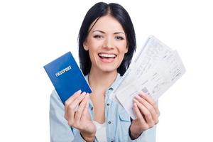 Let us travel Beautiful young smiling woman holding tickets and passport while standing against white background photo