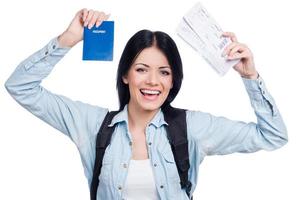 Finally, I am going on vacation  Beautiful young smiling woman holding tickets and passport while standing against white background photo