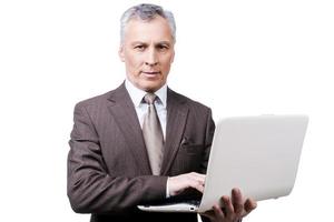 Always busy. Handsome mature man in formalwear adjusting holding laptop while standing against white background photo