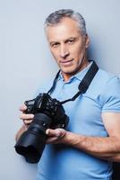 Favorite activity brings maximum pleasure. Portrait of confident senior man in T-shirt holding camera while standing against grey background photo