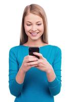 Typing a message to you. Young women holding the mobile phone and smiling while standing against white background photo