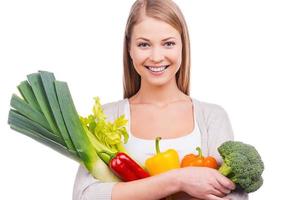 We are what we eat. Beautiful young woman holding different vegetables in hands and looking at camera while standing against white background photo