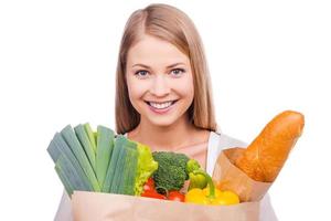 Beautiful buyer. Beautiful young woman carrying a shopping bag full of groceries and looking at camera while standing against white background photo