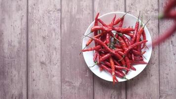 les piments de Cayenne rouges tombent sur une assiette de plus de poivrons video