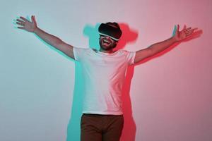 hombre feliz en anteojos de realidad virtual gesticulando con sombras coloridas en el fondo foto