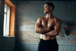 Handsome muscular man keeping arms crossed while standing in gym photo