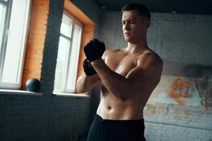 Confident muscular man wearing sport gloves while standing in gym photo