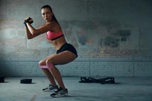 Confident young woman using elastic resistance band while exercising in gym photo