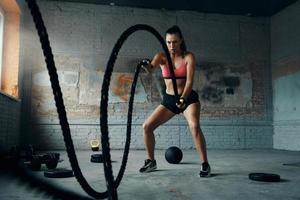 Concentrated young woman exercising with battle rope in gym photo