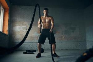 Concentrated young man exercising with battle rope in gym photo