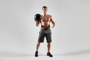Confident young man with perfect body holding medicine ball against white background photo