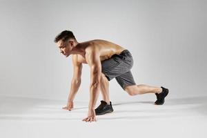 Young fit man preparing to run while standing in starting position against white background photo