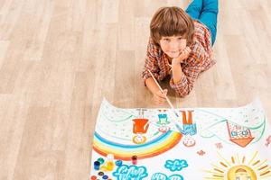 Looking for inspiration. Young boy relaxing while painting with watercolors lying on the floor photo