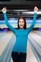 This is strike Beautiful young women keeping arms raised while standing against bowling alleys photo