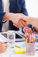 Sealing a deal. Close-up of business people in smart casual wear shaking hands while sitting at the table together photo