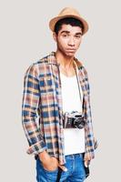 Confident photographer. Handsome young Afro-American hipster holding hands in the pockets and looking at camera while standing against grey background photo