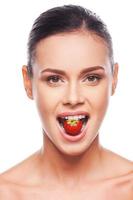 Nutrients for a body and skin. Beautiful young shirtless woman holding strawberry in her mouth while standing against white background photo