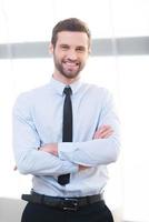 Confident business expert. Confident young businessman keeping arms crossed and smiling while standing indoors photo