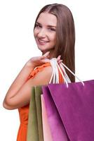 Beautiful shopaholic. Portrait of a beautiful young woman looking over shoulders and holding shopping bags while standing against white background photo
