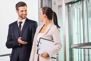 Discussing project with colleague. Two cheerful business people discussing something and smiling while getting out from elevator photo