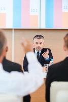 Everyone is welcome for discussion. Confident mature man in formalwear giving a word to someone from audience while sitting in conference hall photo