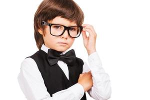 Little Nerd. Cute little boy adjusting his glasses and looking at camera while standing isolated on white photo