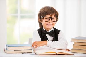 Smart and confident schoolboy. Cute young boy keeping arms crossed while sitting at the table photo