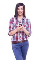 Beauty with mobile phone. Attractive young woman holding mobile phone and smiling at camera while standing isolated on white photo