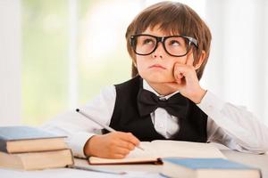 Day dreaming. Bored young boy leaning his face on hand and looking away while sitting at the desk photo