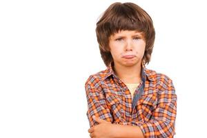 niño travieso. niño triste con los brazos cruzados mientras está de pie aislado en blanco foto