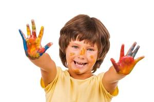 pequeño artista niño feliz mostrando sus palmas recubiertas de pintura colorida mientras está aislado en blanco foto