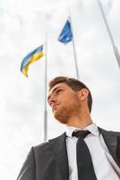 empresario ucraniano. vista de ángulo bajo de un joven confiado en ropa formal con banderas ucranianas y europeas en el fondo foto