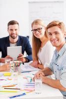 Confident and creative. Group of cheerful business people in smart casual wear sitting together at the table and looking at camera photo