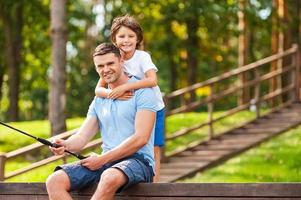 Spending good time with father. Happy father and son fishing together and smiling while sitting on quayside photo