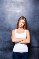 Confused beauty. Beautiful young woman keeping arms crossed while standing against blackboard photo