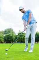 Putting green. Full length of young man in sports clothing playing golf while standing on green photo