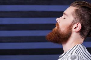 Perfect beard. Side view of handsome young bearded man holding hand on chin while standing against stripped background photo