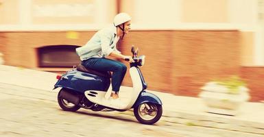 paseo en scooter. vista lateral de un joven con casco montando scooter por la calle y sonriendo foto