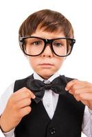 Confident in his skills. Cute little boy adjusting his bow tie and looking at camera while standing isolated on white photo