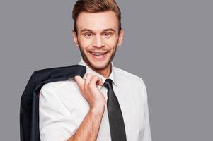 I am confident in everything I do Confident young man in formalwear carrying his jacket on shoulders and looking at camera while standing against grey background photo