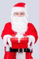 feliz navidad para ti tradicional santa claus estirando la caja de regalo mientras está de pie contra el fondo gris foto