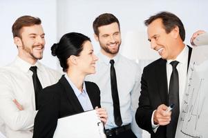 We are making great progress Confident mature businessman pointing graph on whiteboard and smiling while his colleagues standing near him photo