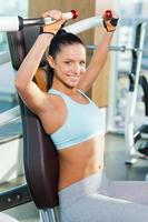 Feeling confident in her perfect body. Attractive young woman looking at camera and smiling while working out in gym photo