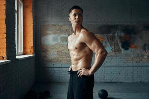 Confident muscular man holding hands on hip while standing in gym photo