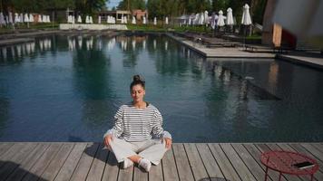 Woman sits cross legged on a dock doing meditative stretches video