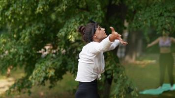 Woman does yoga exercises with others in a park video